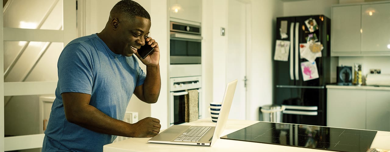 Photo of a man smiling while on the phone, in front of a laptop
